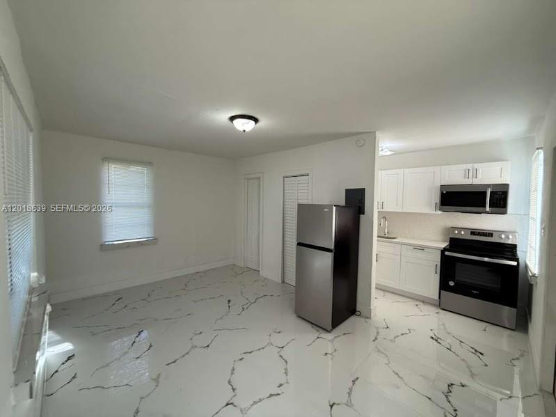 A kitchen and living area with white marble-patterned floors, white cabinets, and stainless steel appliances — 2775 NW 57th St, Miami FL 33142, MIAMI, FL