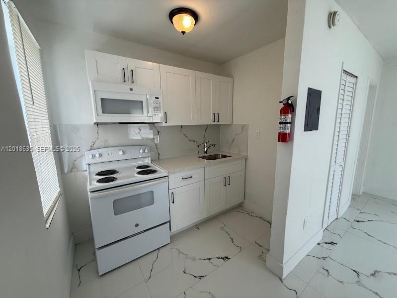 A small kitchen features white cabinets, white appliances, and white marble-patterned tile flooring — 2775 NW 57th St, Miami FL 33142, MIAMI, FL