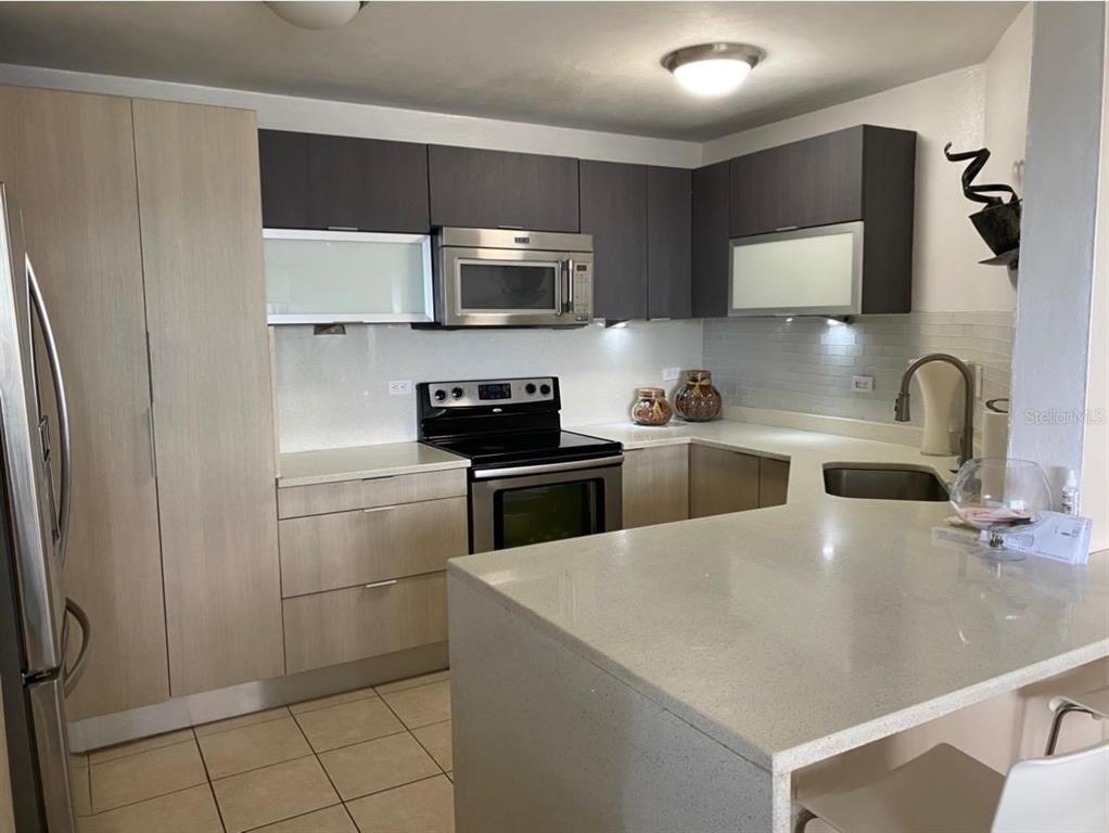 A kitchen features light wood cabinets, dark upper cabinets, stainless steel appliances, and quartz countertops — 155 CARAZO ST. CONDO. REGENCY PARK UNIT 17-C, GUAYNABO, PR