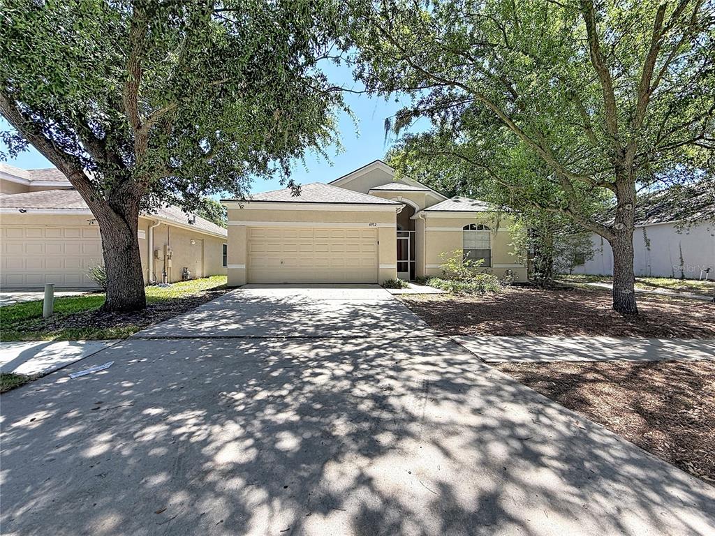 A single-story house with a beige exterior, a two-car garage, and large shade trees — 6932 MONARCH PARK DRIVE, APOLLO BEACH, FL