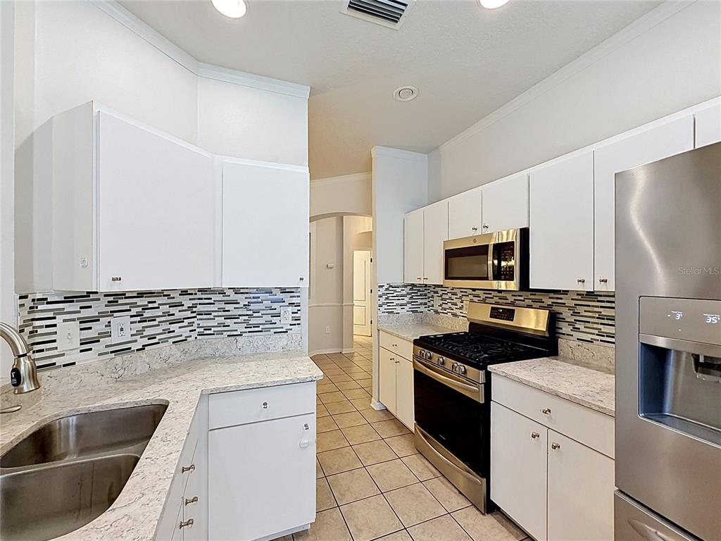 A kitchen features white cabinets, granite countertops, a tiled backsplash, and stainless steel appliances — 6932 MONARCH PARK DRIVE, APOLLO BEACH, FL