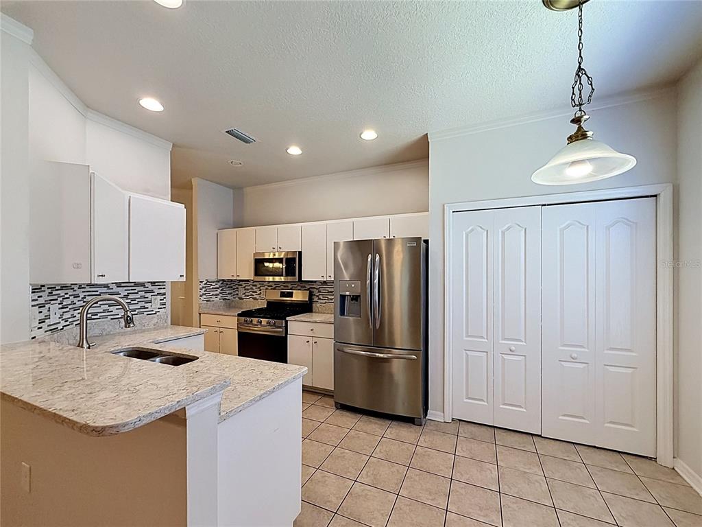 A kitchen features white cabinets, granite countertops, stainless steel appliances, and tile flooring — 6932 MONARCH PARK DRIVE, APOLLO BEACH, FL