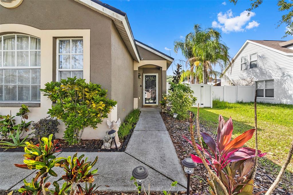 A concrete walkway leads to the front entrance of a house with a landscaped yard — 1239 AVONWOOD COURT, LUTZ, FL
