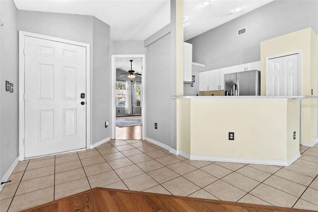 An entryway with tile flooring leads to a kitchen with a breakfast bar and cabinets — 1239 AVONWOOD COURT, LUTZ, FL