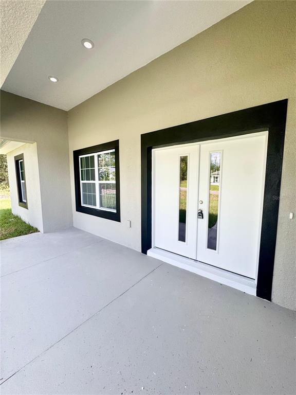 A covered concrete patio features a double front door and a window with black trim — 8051 N PINKINZ WAY, CITRUS SPRINGS, FL