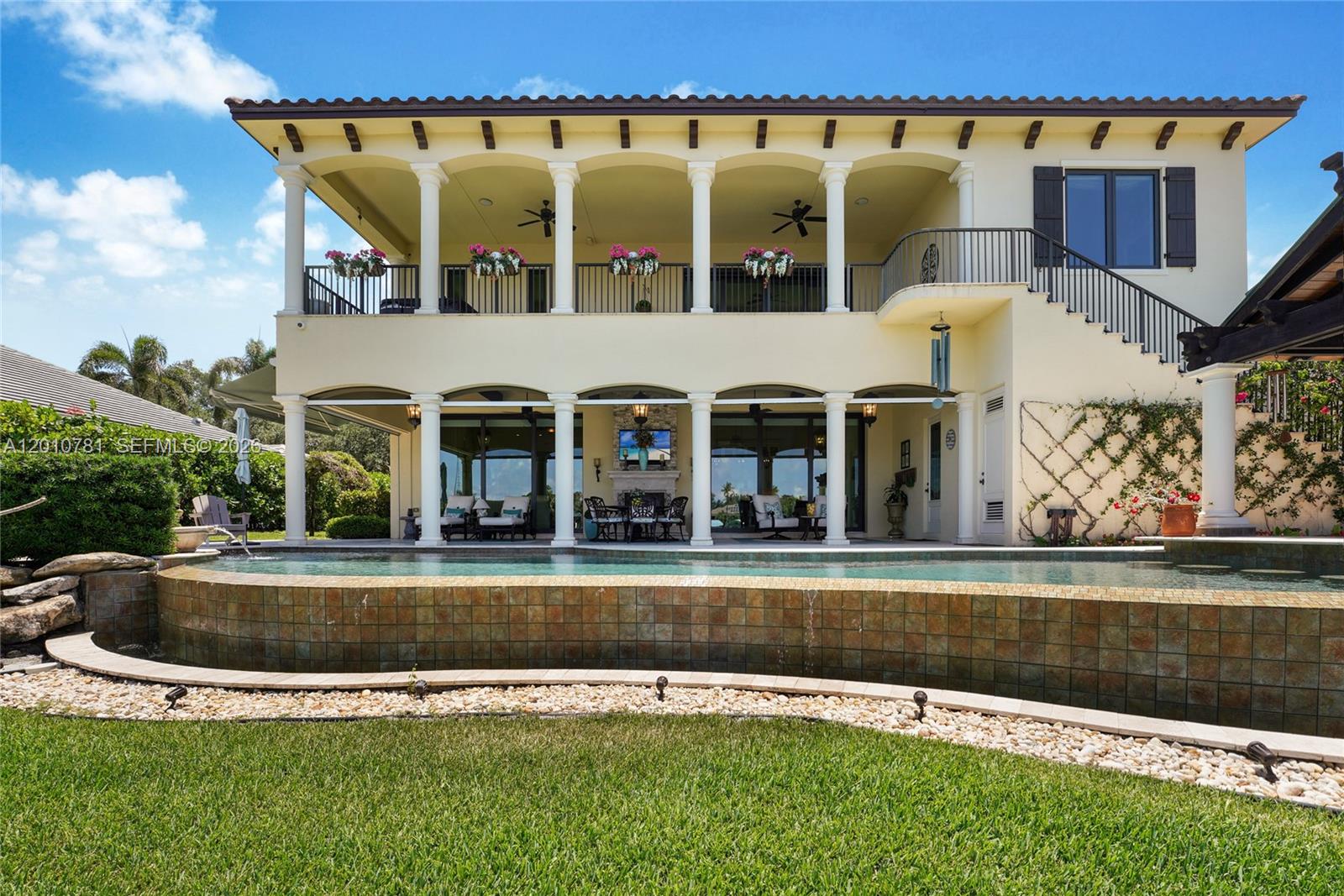 A two-story house with a balcony, covered patio, and an infinity pool overlooking a lawn — 10433 SE Banyan Way, Jupiter FL 33469, JUPITER, FL
