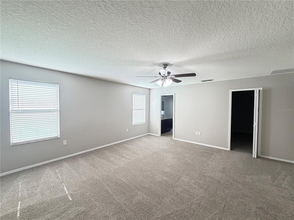 A spacious, carpeted bedroom features light gray walls, three windows with blinds, and a ceiling fan — 14629 BAHAMA SWALLOW BOULEVARD, WINTER GARDEN, FL