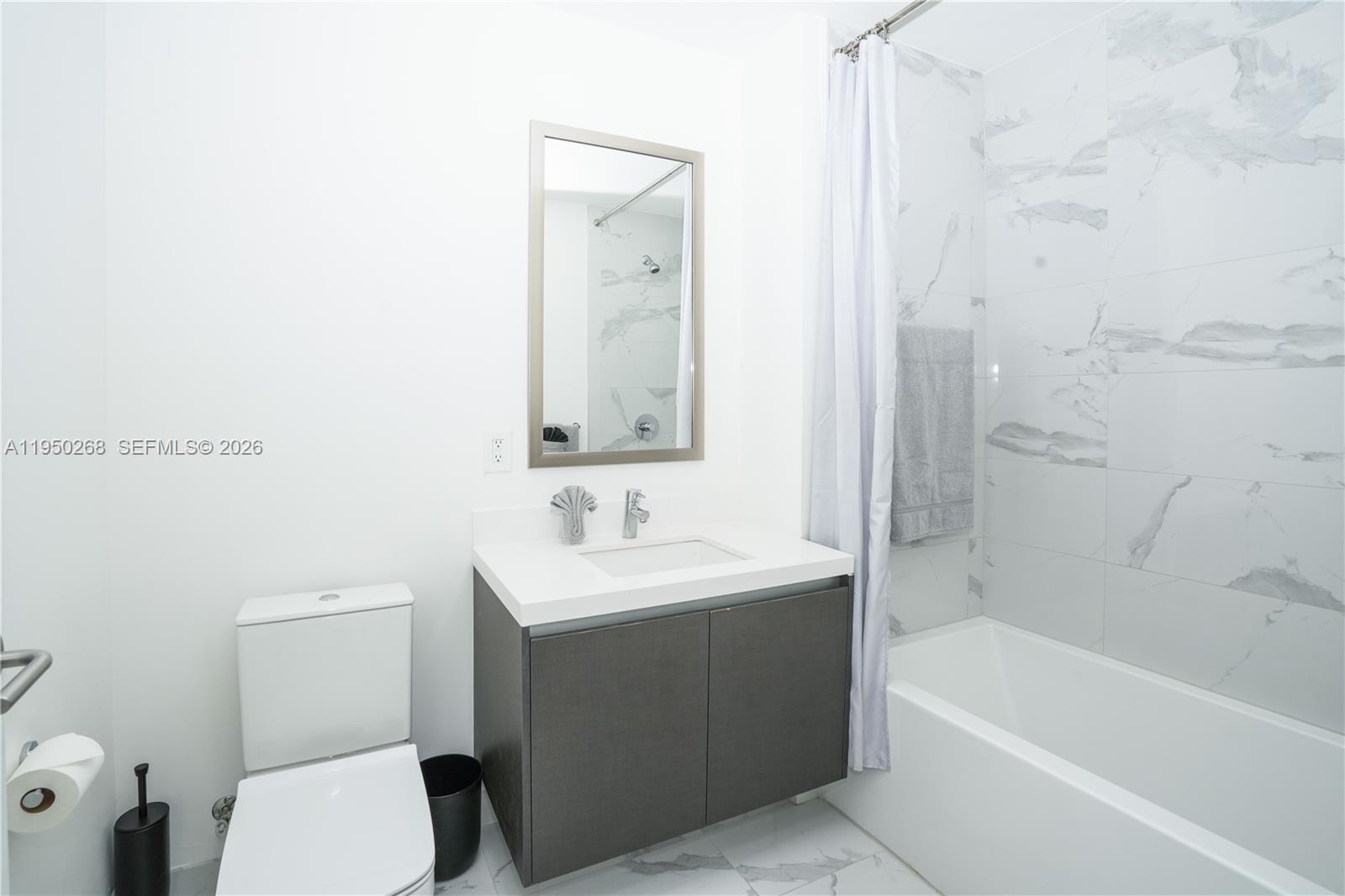 A modern bathroom features a white vanity, a toilet, and a marble-tiled bathtub area — 851 NE 1st Ave # 2101, Miami FL 33132, MIAMI, FL