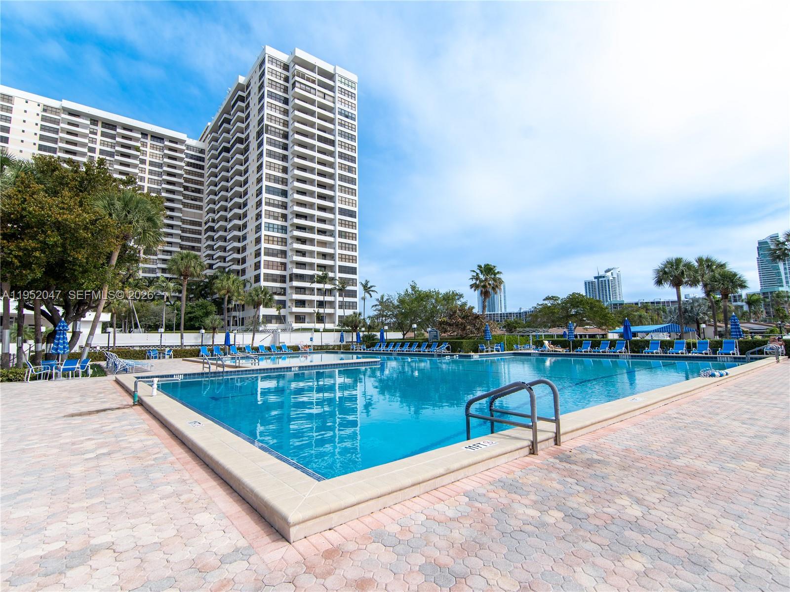 A large outdoor swimming pool sits on a paved deck beside a tall residential building — 2500 Parkview Dr # 2312, Hallandale Beach FL 33009, HALLANDALE BEACH, FL