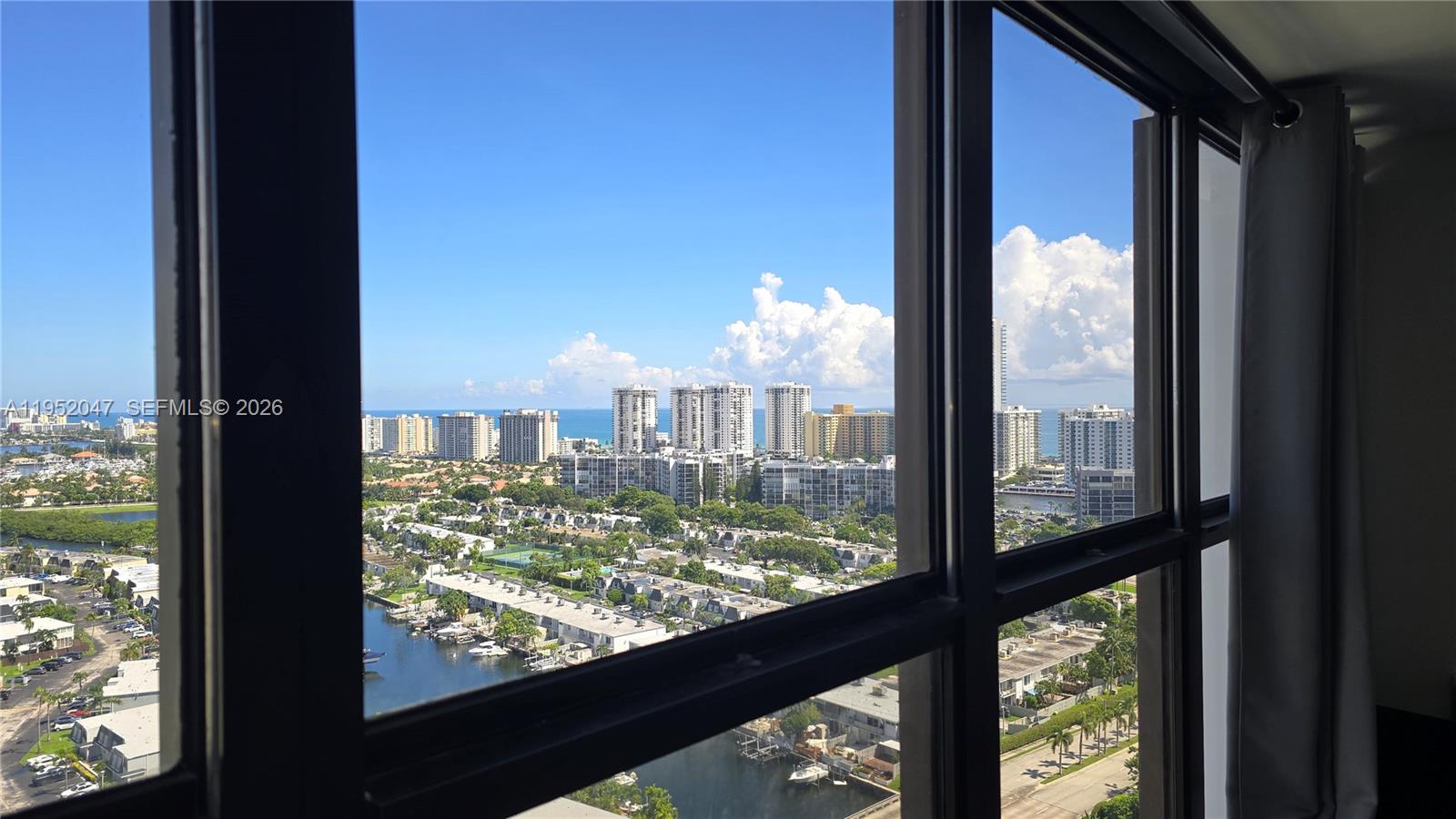 A high-rise view through a window shows a coastal city with buildings, water, and boats — 2500 Parkview Dr # 2312, Hallandale Beach FL 33009, HALLANDALE BEACH, FL