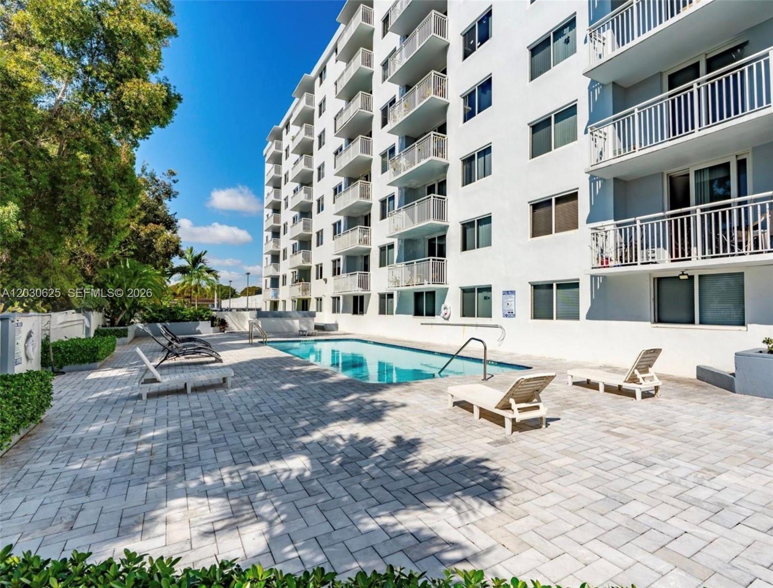A multi-story apartment building overlooks a rectangular swimming pool with a paved patio area — 1251 NE 108th St # 409, Miami FL 33161, MIAMI, FL