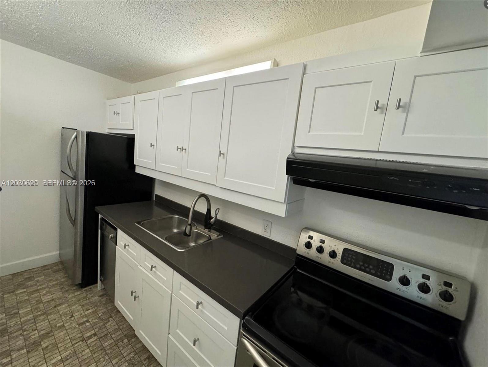 A kitchen features white cabinets, dark countertops, a stainless steel sink, and black appliances — 1251 NE 108th St # 409, Miami FL 33161, MIAMI, FL