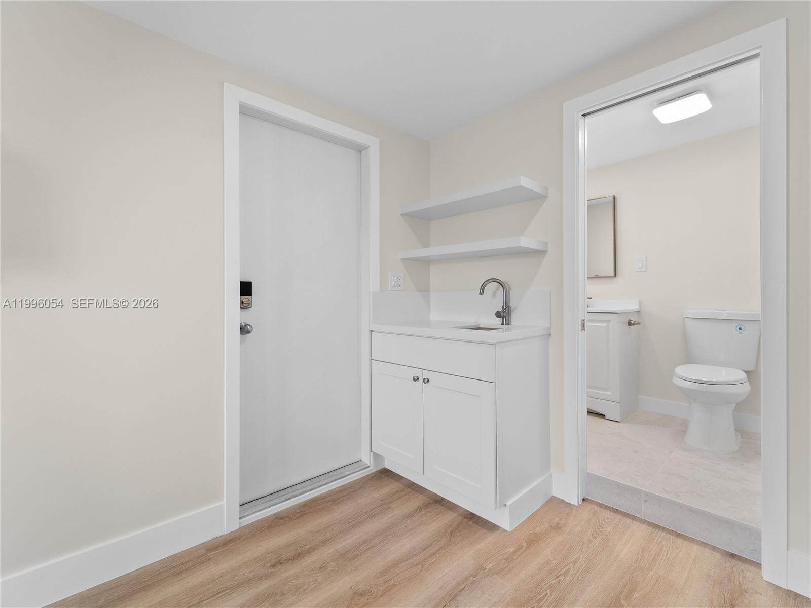 A small wet bar with white cabinets and floating shelves sits beside a bathroom door — 7401 SW 38th St # A, Miami FL 33155, MIAMI, FL
