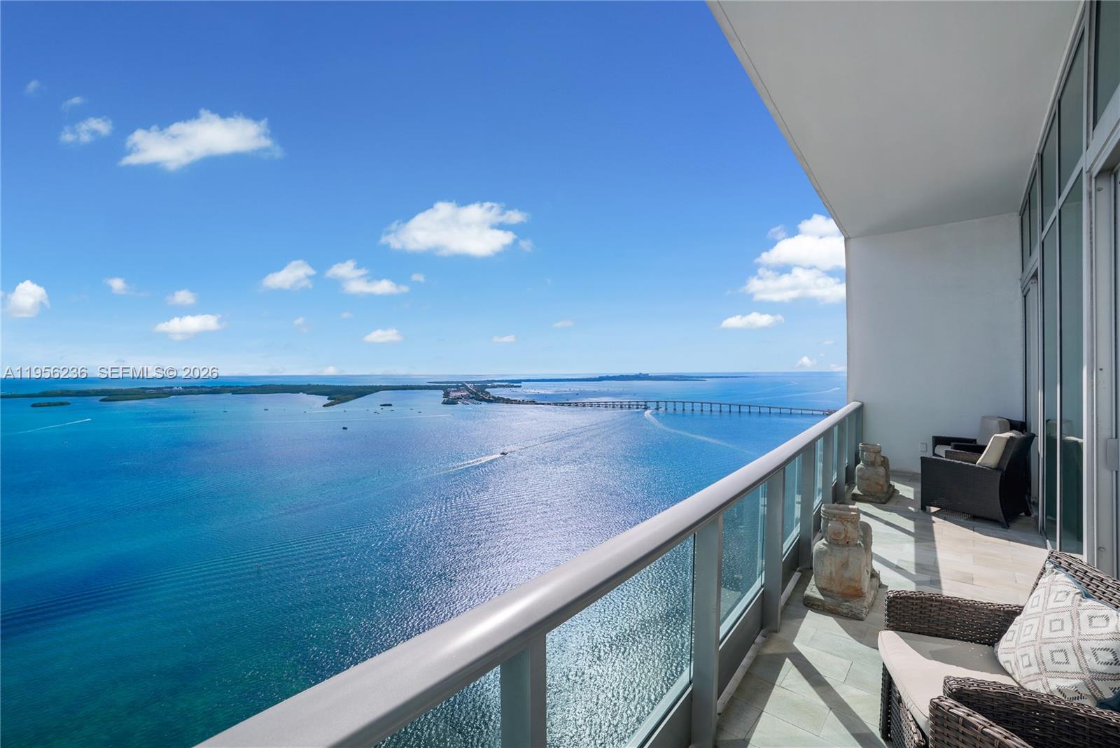 A high-rise balcony features glass railings, wicker furniture, and a panoramic ocean view — 1331 Brickell Bay Dr, Miami FL 33131, MIAMI, FL