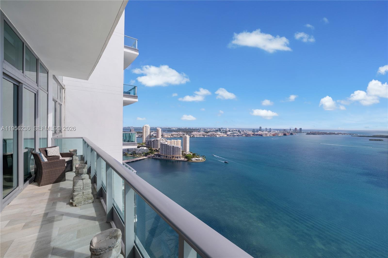 A high-rise balcony with wicker furniture overlooks a bay and a distant city skyline — 1331 Brickell Bay Dr, Miami FL 33131, MIAMI, FL