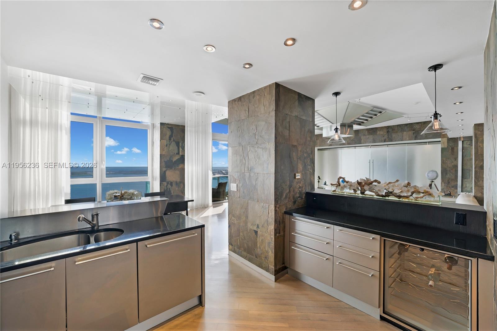 A modern kitchen features dark stone walls, black countertops, metallic cabinets, and floor-to-ceiling windows — 1331 Brickell Bay Dr, Miami FL 33131, MIAMI, FL