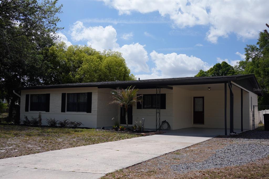 A single-story house with a carport, light-colored siding, and dark shutters under a cloudy sky — 1120 SAN LUIS DRIVE, ORLANDO, FL