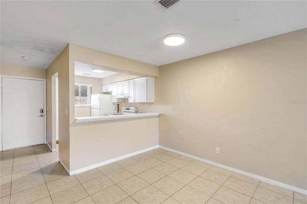 A dining area with tile flooring opens to a kitchen with white cabinets and appliances — 410 BUTLER BOULEVARD, DAYTONA BEACH, FL