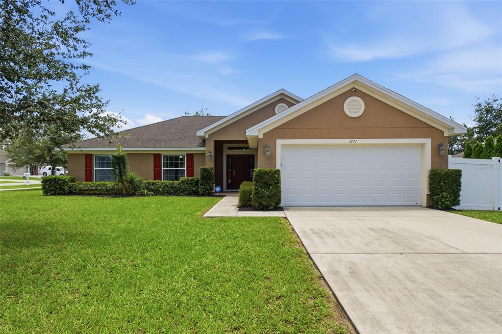 A single-story tan house with a two-car garage, red shutters, and a green lawn — 3777 FANTASY WAY, BROOKSVILLE, FL