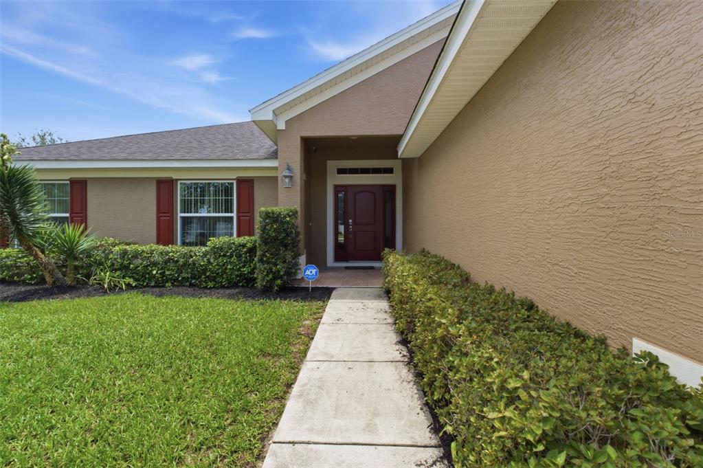 A concrete walkway leads to the front entrance of a tan house with red shutters — 3777 FANTASY WAY, BROOKSVILLE, FL