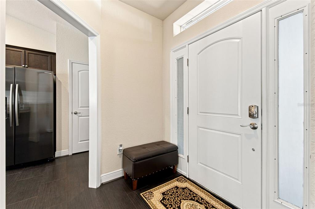 An entryway features a white front door with sidelights, a dark storage bench, and tile flooring — 3777 FANTASY WAY, BROOKSVILLE, FL