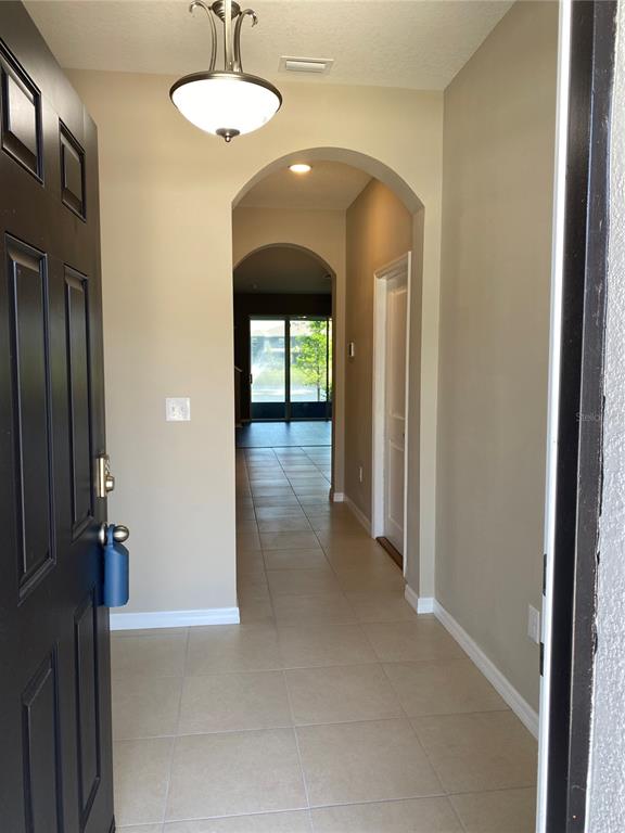 An entryway with tile flooring leads through an arched hallway toward a rear sliding door — 8642 FALLING BLUE PLACE, RIVERVIEW, FL