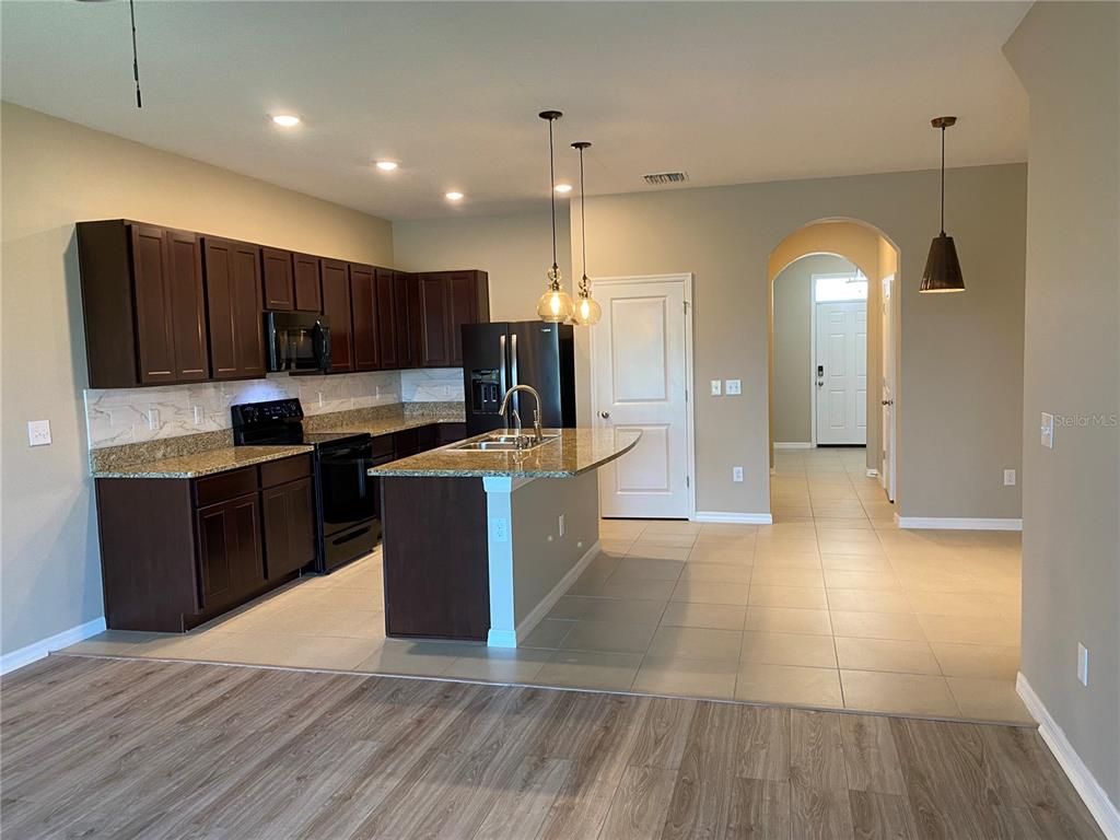A kitchen features dark wood cabinets, granite countertops, a center island, and tile flooring — 8642 FALLING BLUE PLACE, RIVERVIEW, FL