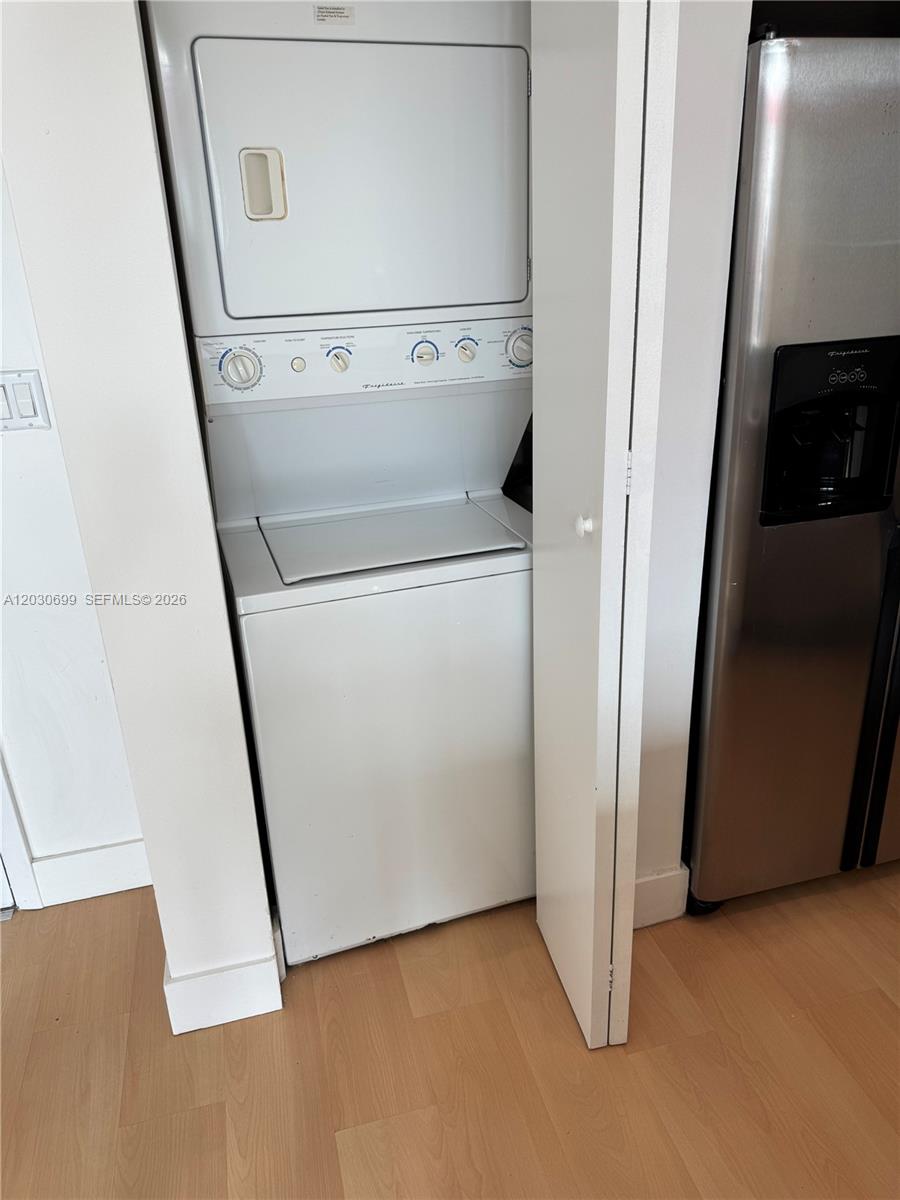 A white stacked washer and dryer unit sits in a closet next to a refrigerator — 350 NE 24th St # 407, Miami FL 33137, MIAMI, FL