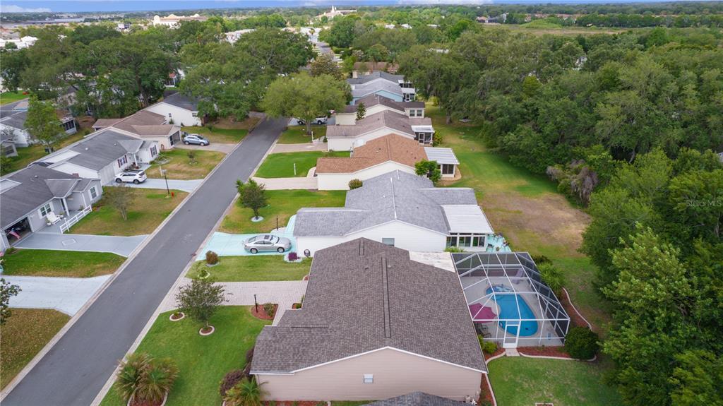An aerial view shows a suburban street with single-family homes, driveways, and a screened pool — 1411 JUAREZ PLACE, THE VILLAGES, FL