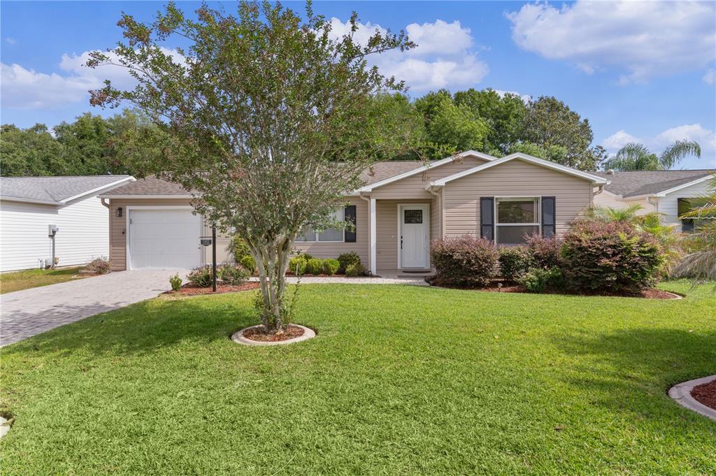 A single-story house with beige siding, a white front door, and a paved driveway — 1411 JUAREZ PLACE, THE VILLAGES, FL