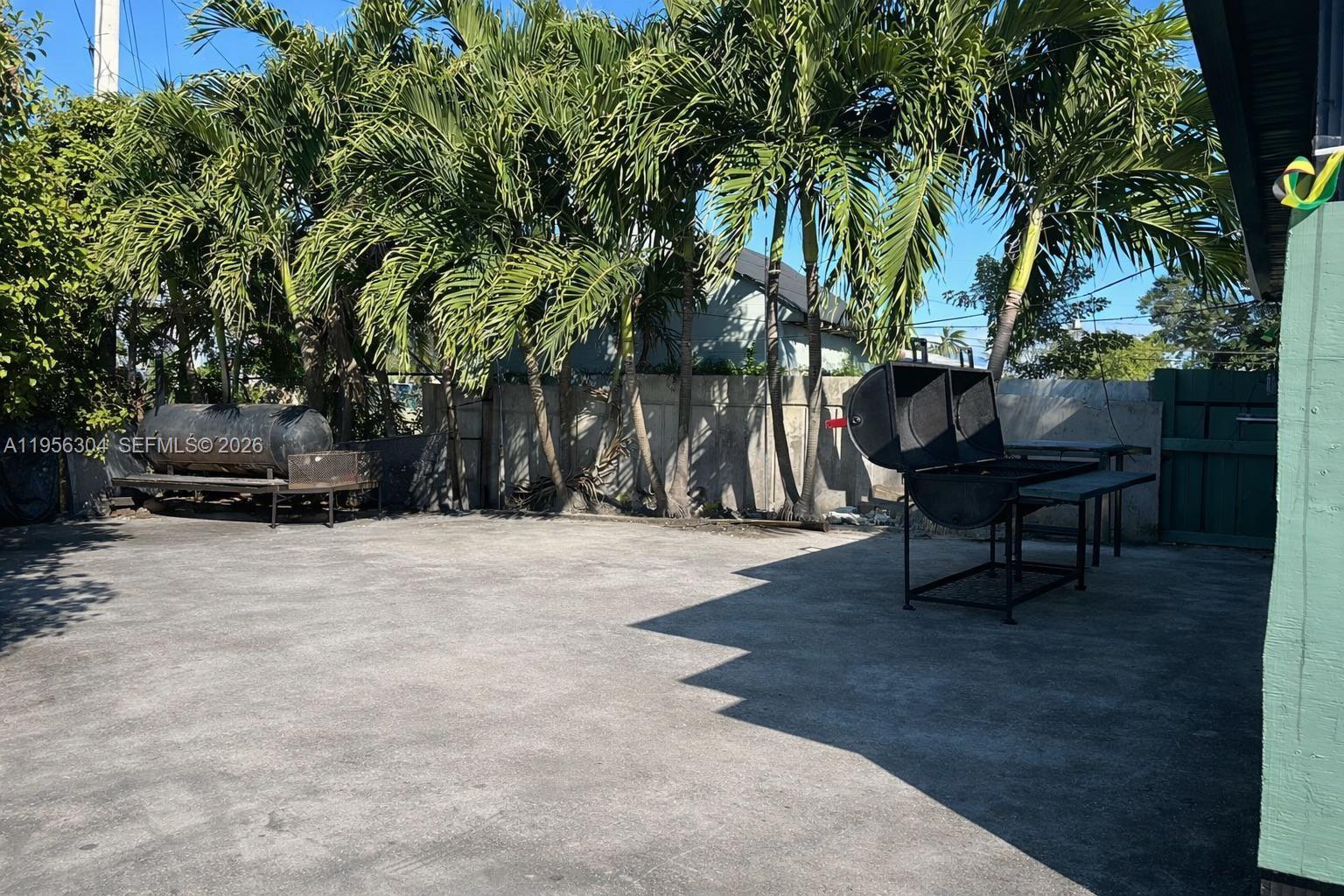A concrete patio features two large outdoor grills and several palm trees against a wall — 21855 S Dixie Hwy, Miami FL 33170, MIAMI, FL