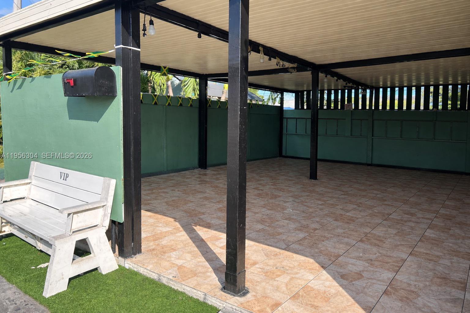 A covered outdoor patio features tiled flooring, black support columns, and a green privacy fence — 21855 S Dixie Hwy, Miami FL 33170, MIAMI, FL