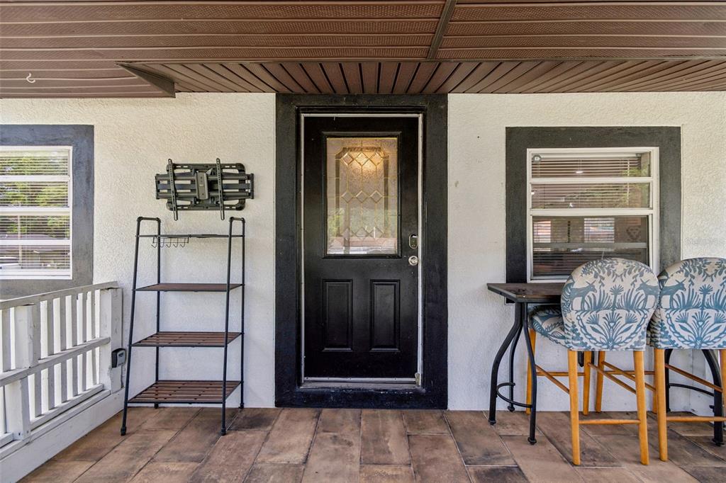 A covered porch features a black front door, a metal shelving unit, and two chairs — 1202 E ANNIE STREET, TAMPA, FL