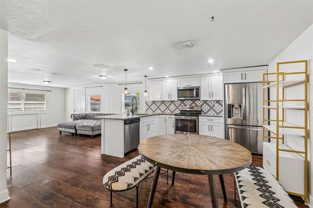 An open-concept kitchen and living area features white cabinetry, stainless steel appliances, and wood flooring — 1202 E ANNIE STREET, TAMPA, FL