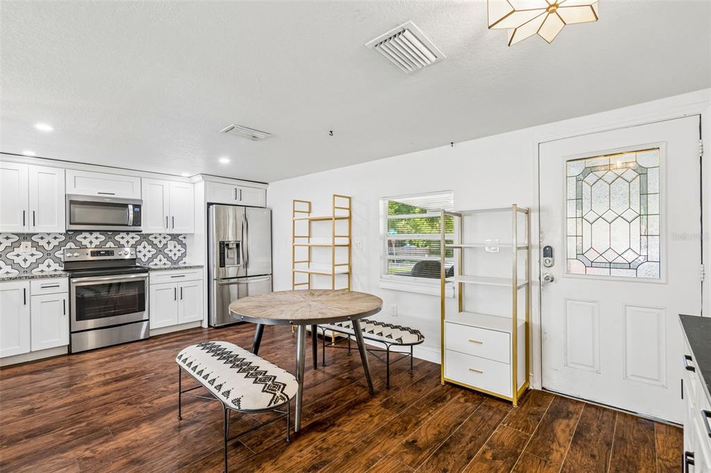 A kitchen with white cabinets, stainless steel appliances, patterned backsplash, and a round dining table — 1202 E ANNIE STREET, TAMPA, FL