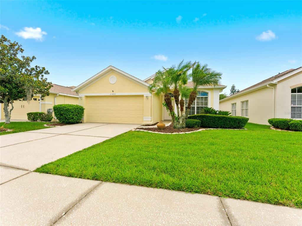 A single-story yellow house with a two-car garage and a manicured front lawn — 23802 CORAL RIDGE LANE, LAND O LAKES, FL