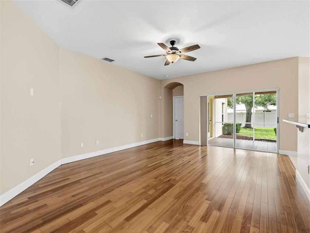 An empty living room features hardwood floors, a ceiling fan, and sliding glass patio doors — 23802 CORAL RIDGE LANE, LAND O LAKES, FL