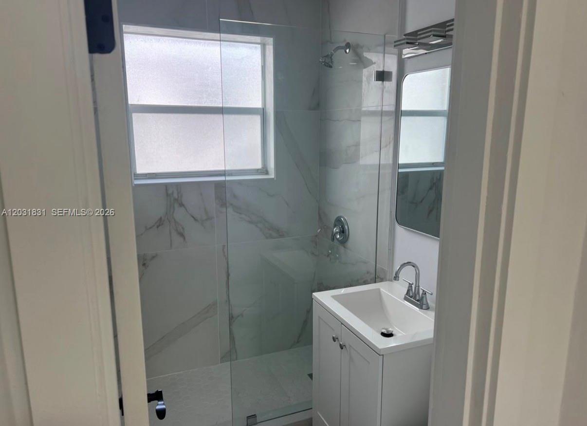A modern bathroom features a glass-enclosed shower with marble-style tile and a white vanity — 7730 Byron Ave # 4, Miami Beach FL 33141, MIAMI BEACH, FL