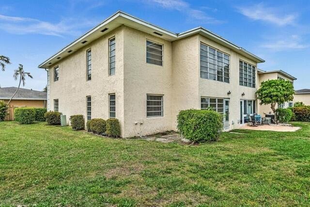 A two-story, light-colored stucco building sits on a grassy lawn under a blue sky — 13721 Flora Place # D, Delray Beach FL 33484, DELRAY BEACH, FL