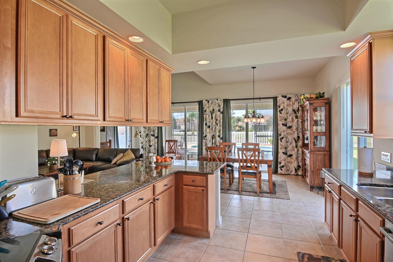 A kitchen with light wood cabinets and granite countertops overlooks a dining area and patio — 5254 Eleuthra Circle, Vero Beach FL 32967, VERO BEACH, FL