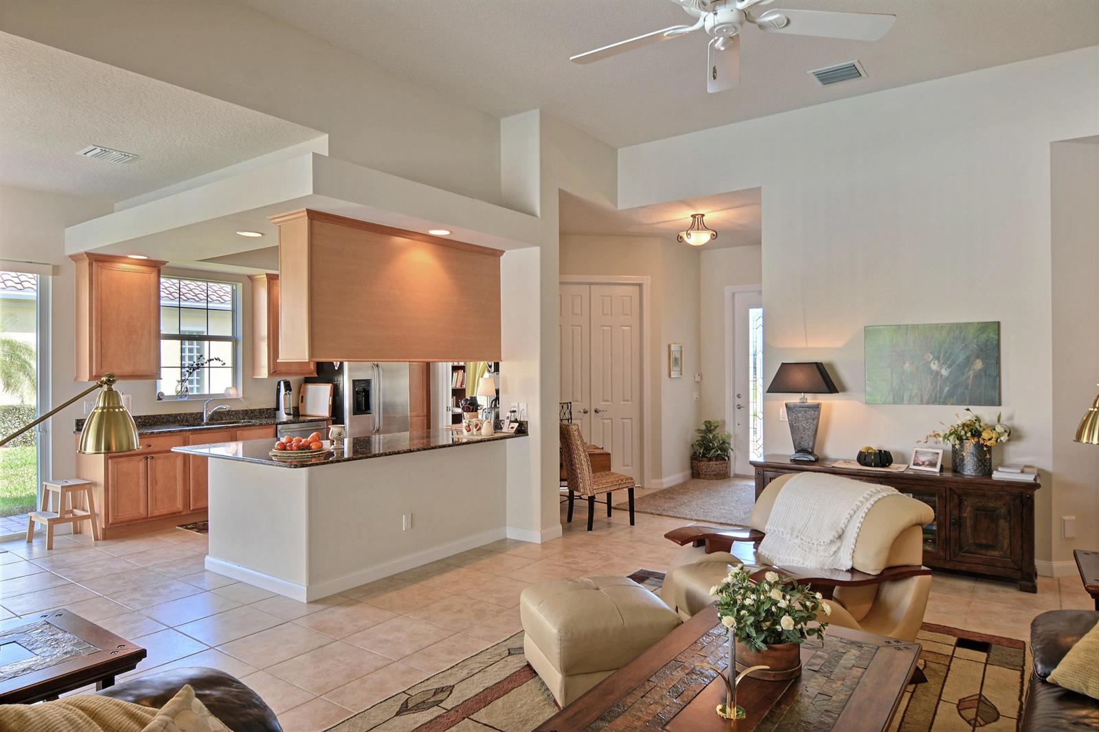An open-concept kitchen with wood cabinets and a granite island overlooks a living room area — 5254 Eleuthra Circle, Vero Beach FL 32967, VERO BEACH, FL