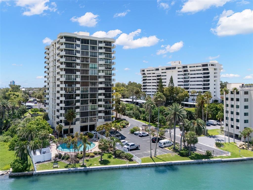 An aerial view shows three multi-story residential buildings near a pool and a waterfront — 80 ROGERS STREET UNIT 3A, CLEARWATER, FL