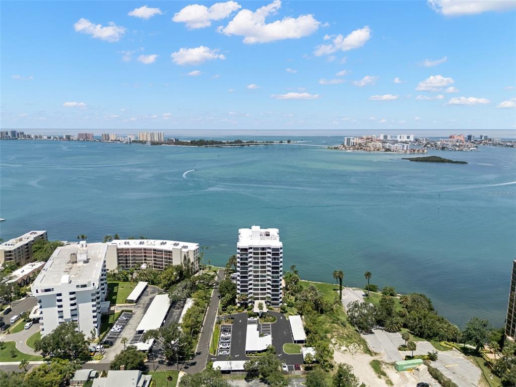 An aerial view shows high-rise apartment buildings along a waterfront with a bridge in the distance — 80 ROGERS STREET UNIT 3A, CLEARWATER, FL