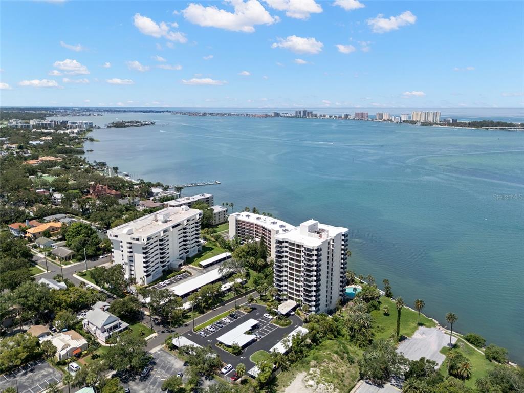 An aerial view shows two white high-rise apartment buildings situated along a large bay — 80 ROGERS STREET UNIT 3A, CLEARWATER, FL
