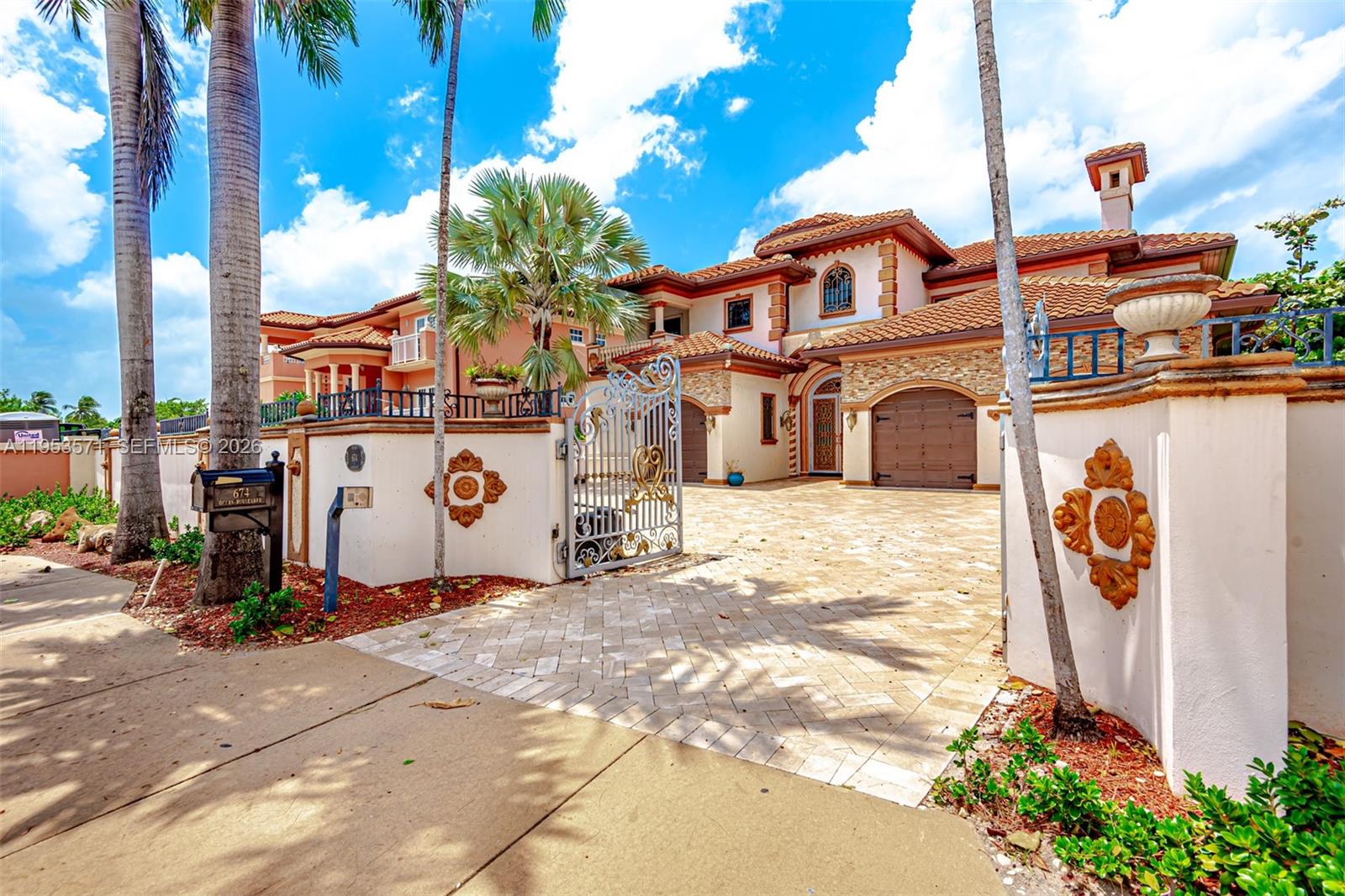 A large Mediterranean-style house with a tiled roof, stone accents, and a gated paved driveway — 674 Ocean Blvd, Golden Beach FL 33160, GOLDEN BEACH, FL