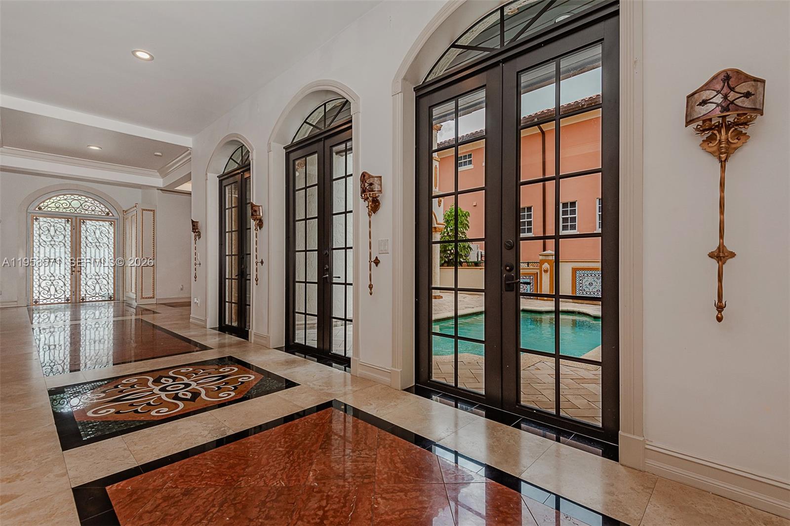A tiled hallway features arched glass doors opening to a patio with a swimming pool — 674 Ocean Blvd, Golden Beach FL 33160, GOLDEN BEACH, FL