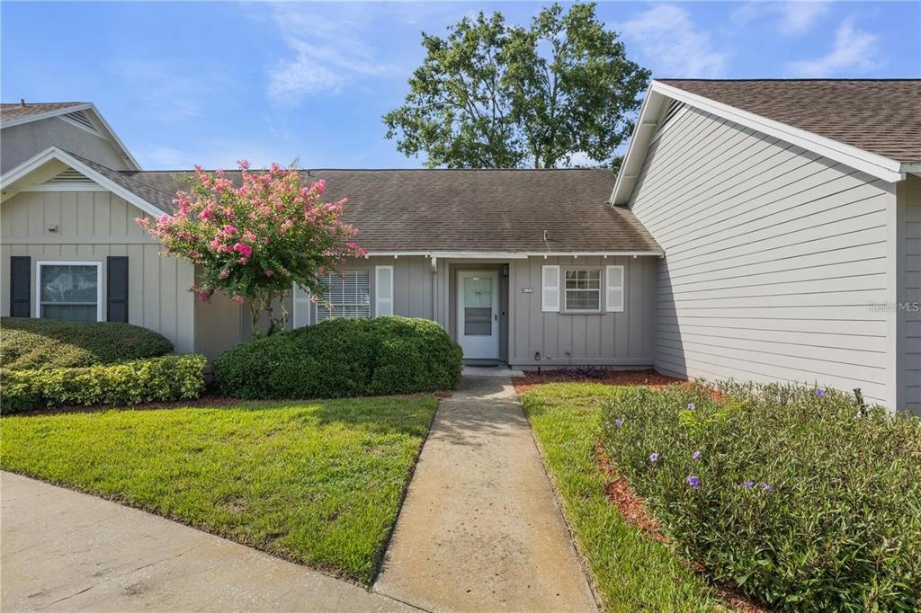 A single-story house with gray siding, a concrete walkway, and a blooming crape myrtle tree — 1134 VILLA LANE UNIT 95, APOPKA, FL