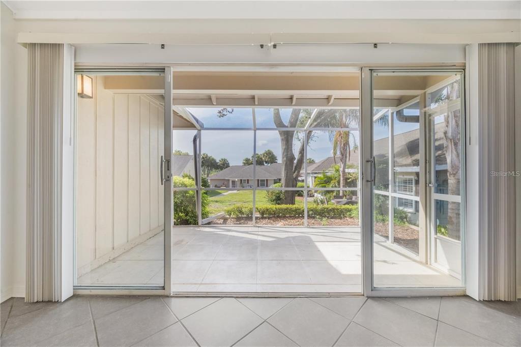 A view through sliding glass doors to a screened-in patio overlooking a residential neighborhood — 1134 VILLA LANE UNIT 95, APOPKA, FL