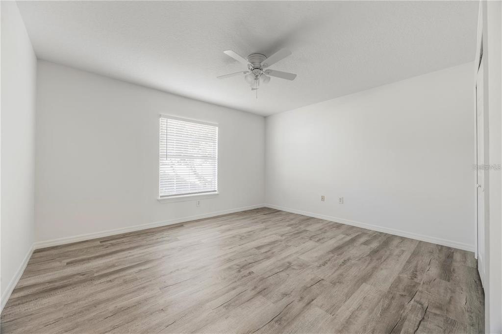 An empty bedroom features white walls, light wood-look flooring, a ceiling fan, and a window — 1134 VILLA LANE UNIT 95, APOPKA, FL