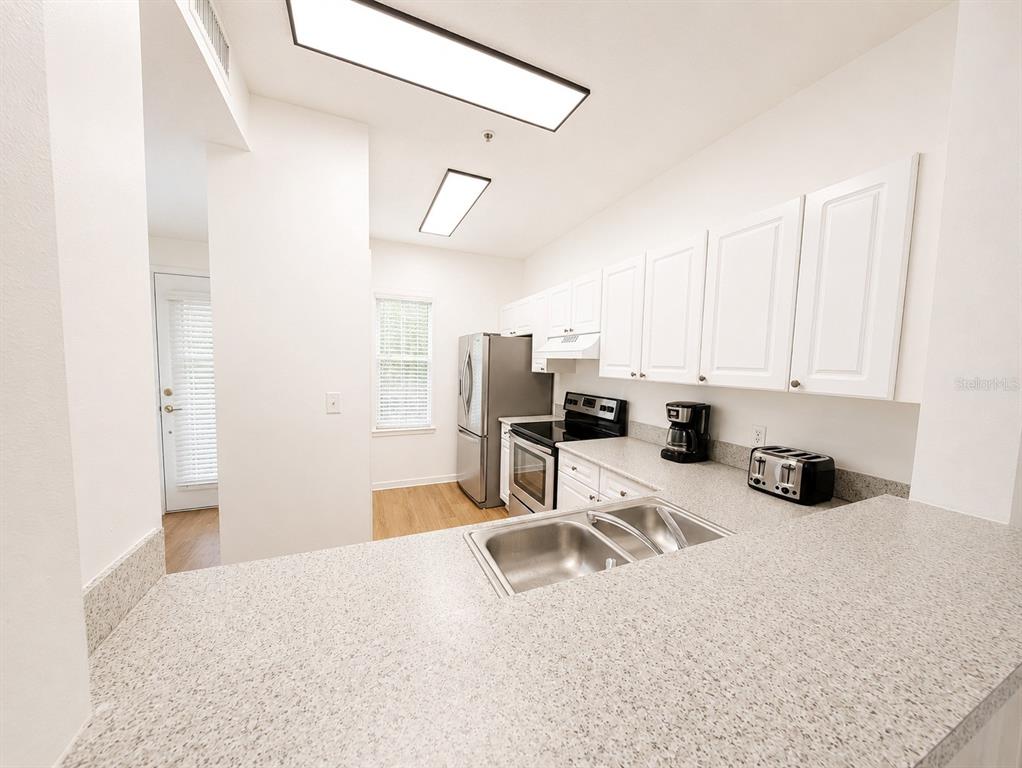 A kitchen features white cabinets, stainless steel appliances, and a speckled countertop with a sink — 660 CELEBRATION AVENUE UNIT 240, KISSIMMEE, FL